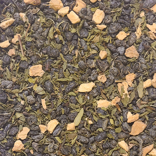 A close up of the Assurance tea blend - dried ginger root and spearmint leaves on a bed of vibrant, bunched up Gunpowder green tea leaves